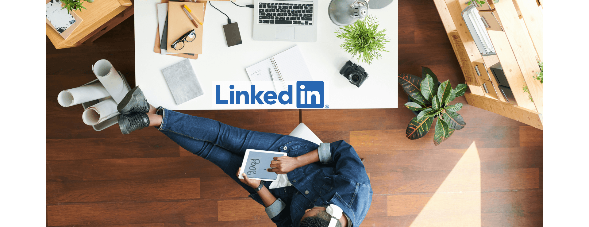 Overhead view of a person sitting at a desk with plants and a laptop, holding a tablet displaying "Post," with LinkedIn logo.
