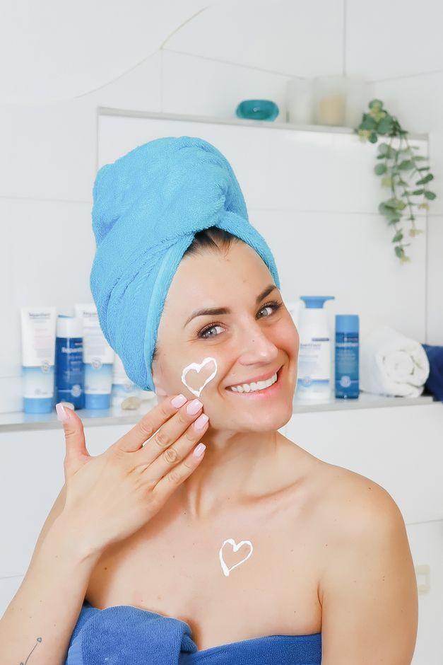 Smiling woman wrapped in a bath towel applying skin care products