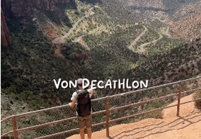 Person standing on a cliff, overlooking a vast canyon landscape with a winding road below under a clear blue sky.