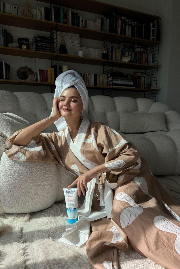 woman sitting in bathrobe presenting skincare product