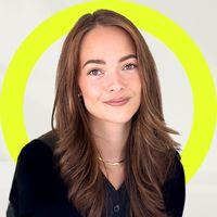 Smiling woman with long brown hair in a black shirt, against a light background with a bright yellow circular accent behind her.